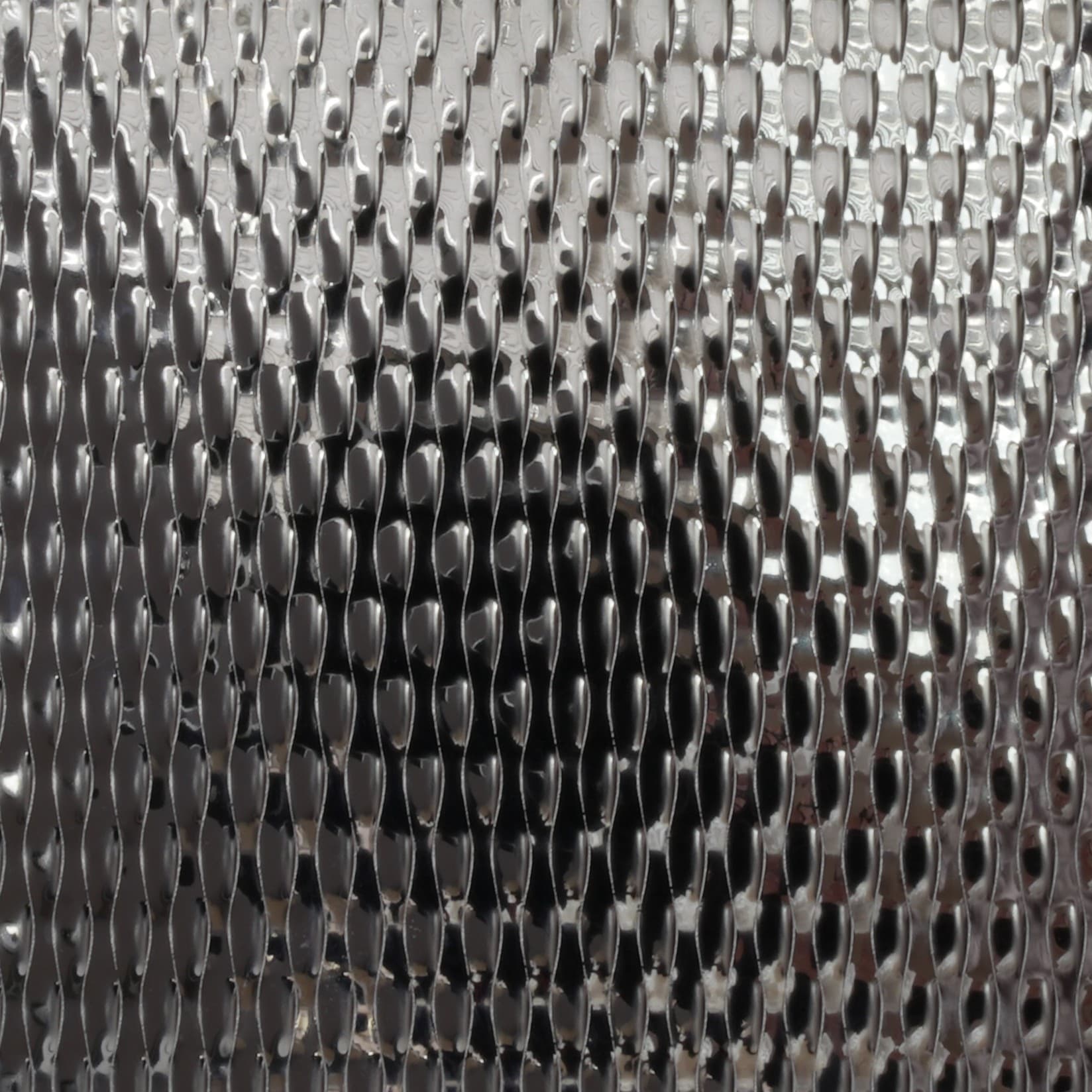 Bright stainless sheet with a fine raised diamond relief, dark reflections across the pattern